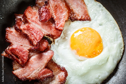 Fényképezés Slices of smoked bacon and fried egg in frying pan