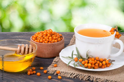 Tea of sea-buckthorn berries with honey on wooden table blurred garden background photo