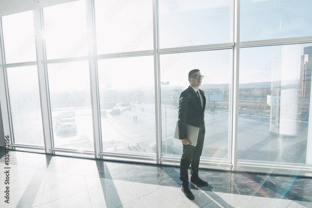 Handsome businessman in suit and eyeglasses move with laptop in hands in office