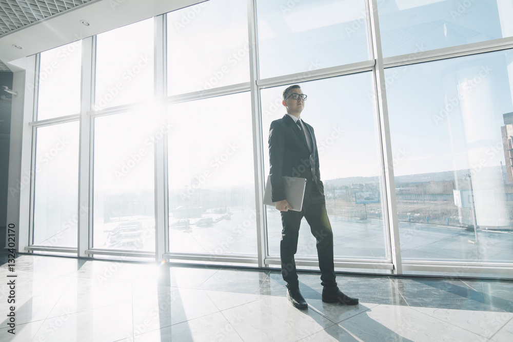 Handsome businessman in suit and eyeglasses move with laptop in hands in office Handsome businessman in suit and eyeglasses move with laptop in hands in office