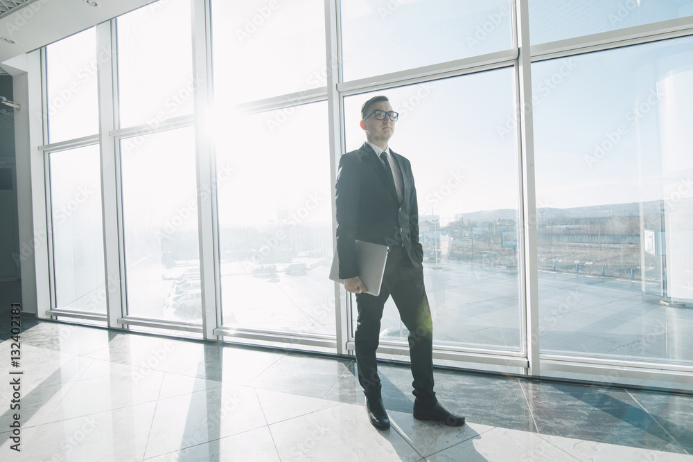 Handsome businessman in suit and eyeglasses move with laptop in hands in office Handsome businessman in suit and eyeglasses move with laptop in hands in office