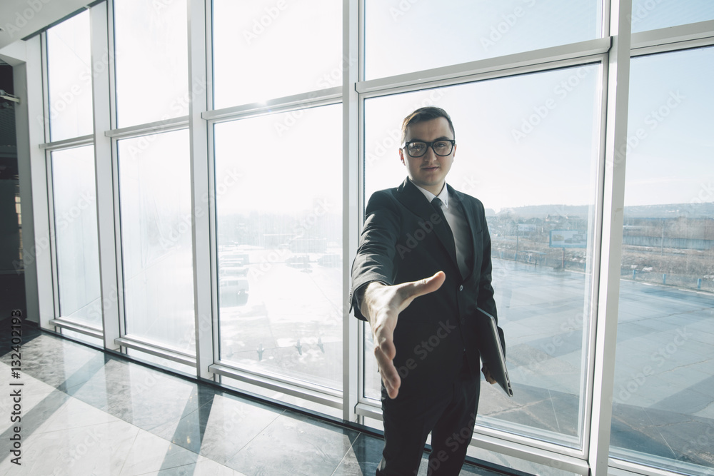 Handsome businessman in suit and eyeglasses give handshake in office room with panoramic windows Handsome businessman in suit and eyeglasses give handshake in office room with panoramic windows