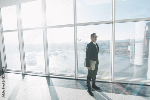 Handsome businessman in suit and eyeglasses move with laptop in hands in office