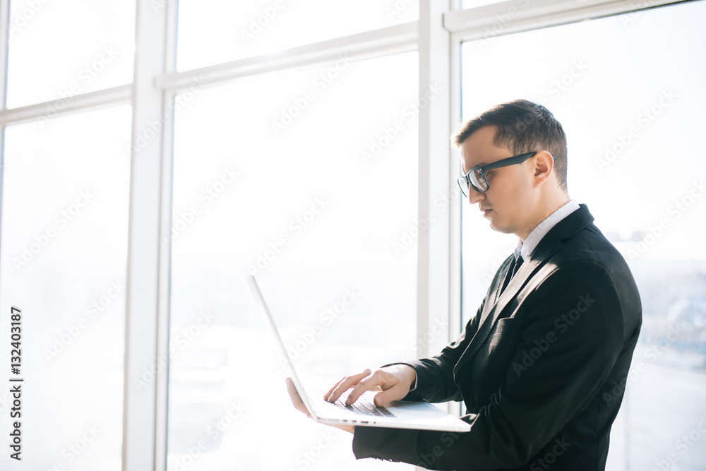 Handsome business man in suit and eyesglasses with laptop against panoramic windows room. Handsome business man in suit and eyesglasses with laptop against panoramic windows room.