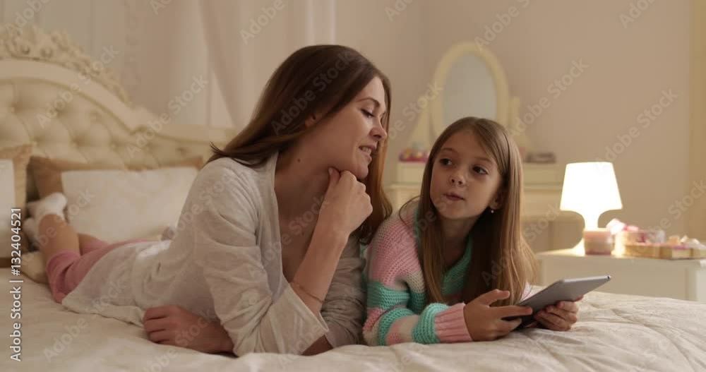 Mother With Daughter Lying On Bed Using Tablet Computer Happy Smiling Young Family Small Girl And Woman Bedroom Mother With Daughter Lying On Bed Using Tablet Computer Happy Smiling Young Family Small Girl And Woman Bedroom