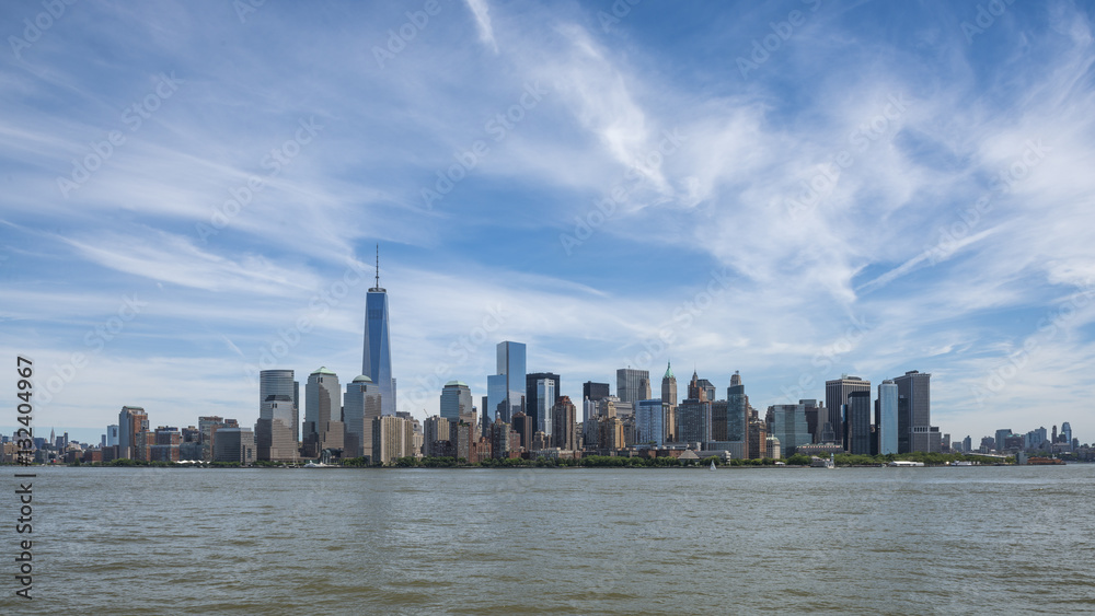 Vista dello skyline di Manhattan, NewYork da sud con il One Trade Center sulla sinistra e un cielo blu con qualche nuvola.