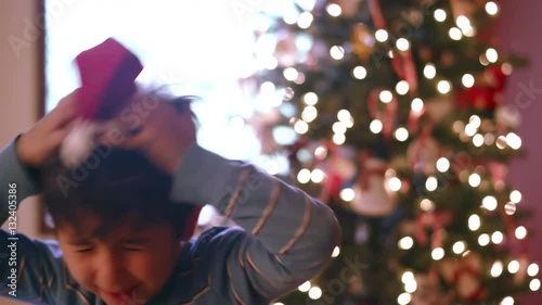 Boy dances with tiny santa hat on and then places it on a miniature christmas tree