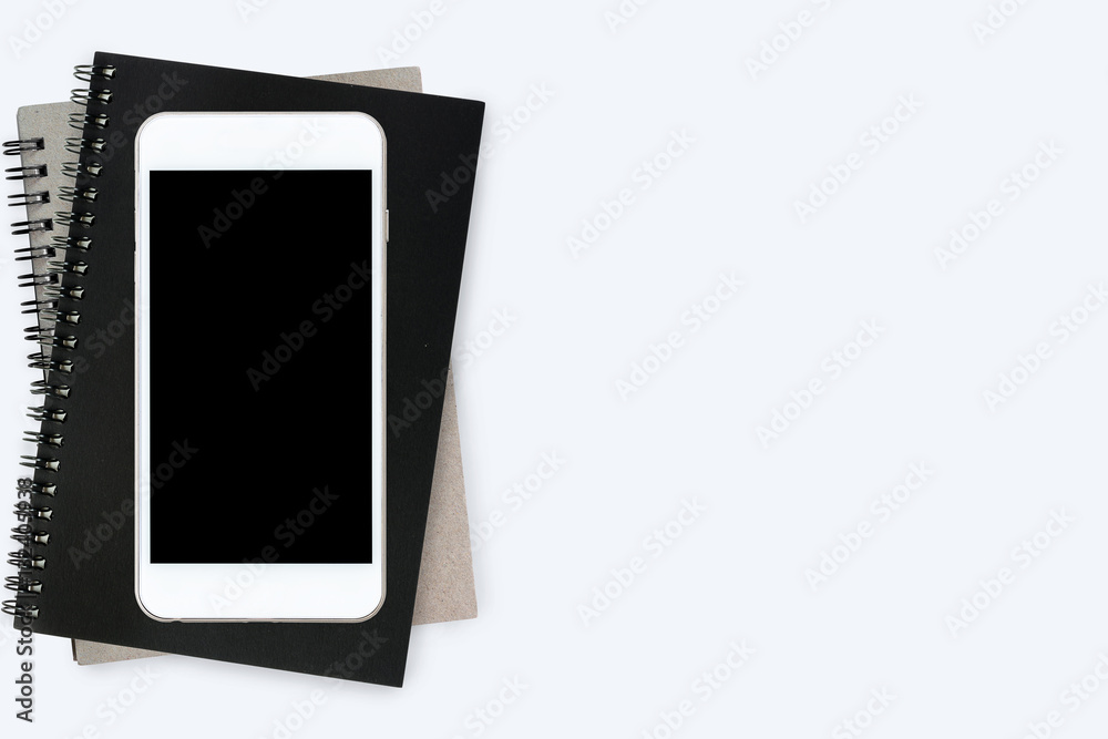 Smartphone with blank screen is on top of notebooks on white table. Top view, flat lay. Smartphone with blank screen is on top of notebooks on white table. Top view, flat lay.