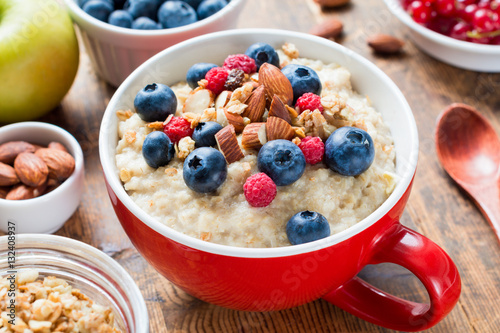 Oatmeal porridge loaded with fresh blueberries, raspberries, almonds and granola on red cup bowl. Healthy breakfast, diet food, healthy eating concept.