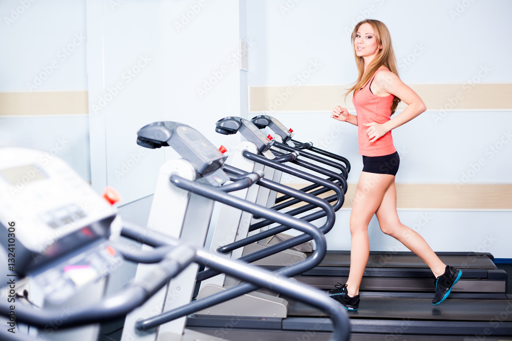 Active young woman running on treadmill at the gym exercising. Run on a machine. Active young woman running on treadmill at the gym exercising. Run on a machine.