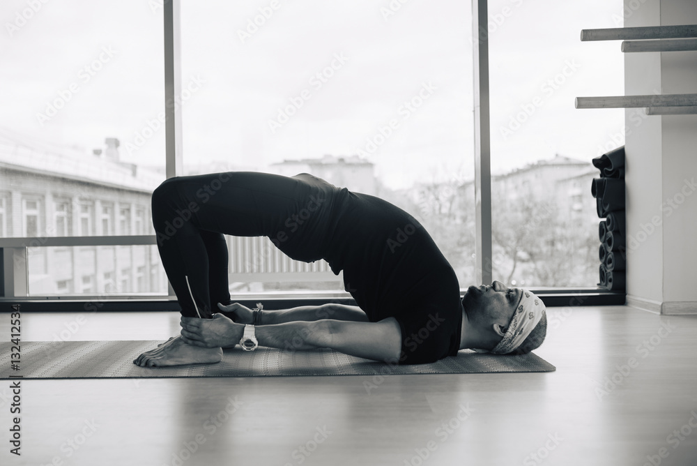 Experienced yoga man doing various  pose and stretching exercises indoors, panoramic city view at background
