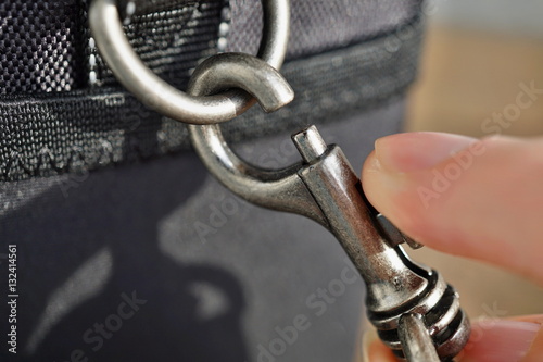 Macro detail of a snap-hook (snap-link) fastened to the black bag with silver loop as a symbol of safety link between two objects