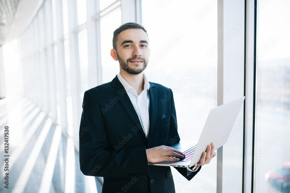 Handsome businessman in suit with laptop in flight terminal Handsome businessman in suit with laptop in flight terminal