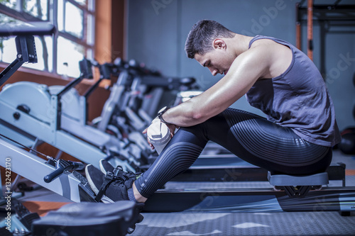 Young man resting on rowing machine in gym