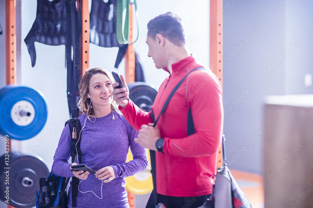 Young man and woman with cell phones and earbuds in gym