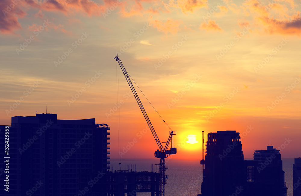Silhouette of construction tower crane with sunset background at evening time.