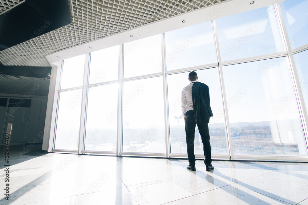 Young relaxed businessman with jacket over shoulders in modern office panoramic windows