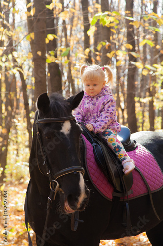 little girl walks in autumn forest with a horse