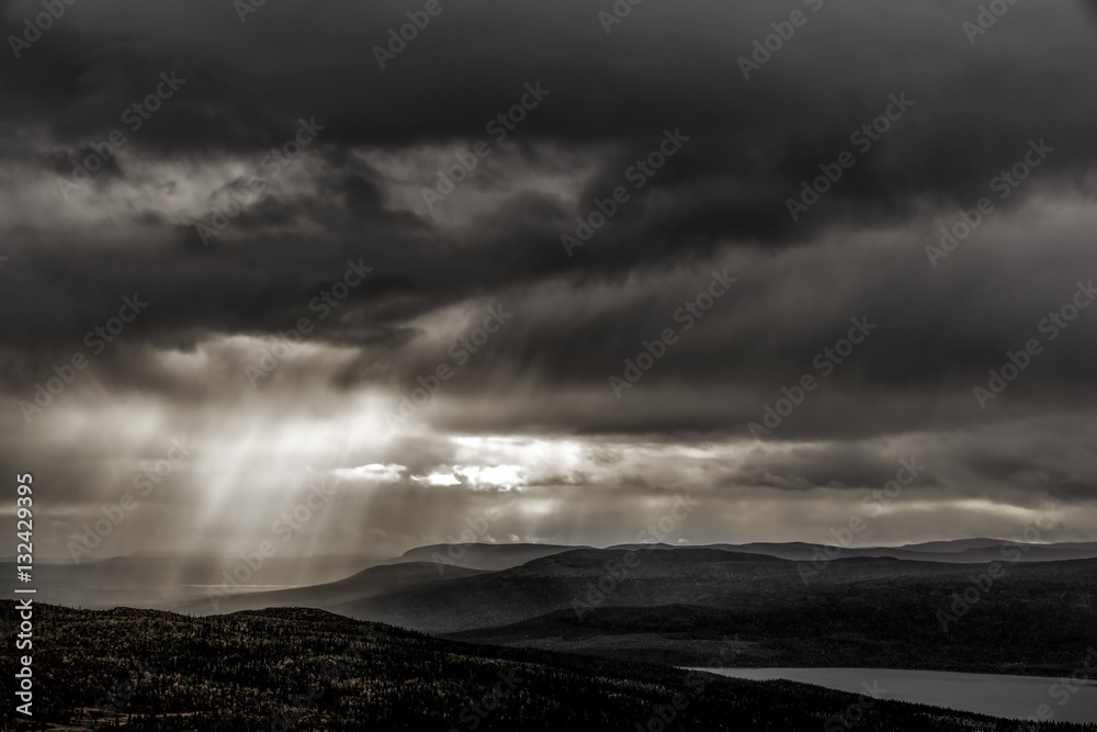 Moody woodland and lake landscape with sun beams comming through rain clouds, Sweden