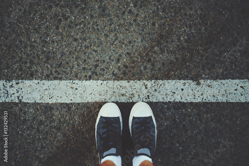 Male feet in white socks and gumshoes standing near grunge white line on gray asphalted road, ready to go