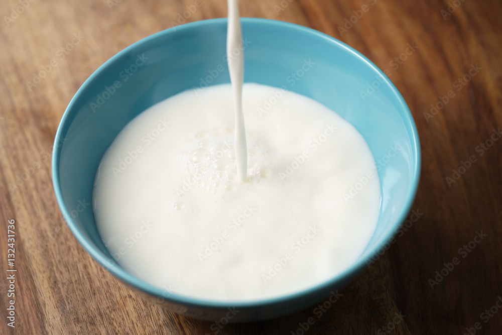 fresh milk poured into blue bowl on wood table, organic food fresh milk poured into blue bowl on wood table, organic food