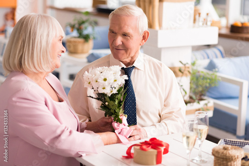 Gallant grey haired man presenting his lady flowers