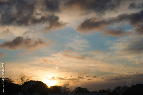 Sunrise over a tree line with a orange sun with some clouds on a bleu sky