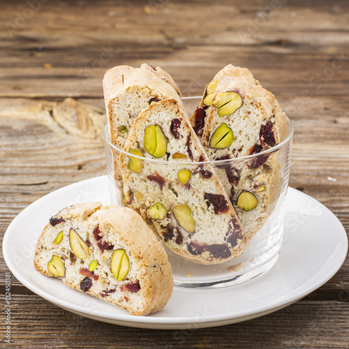 Crispy traditional delicious Italian biscotti cookies or kantuchchi with pistachios and dried cranberries in a glass on  marble background. selective focus photo