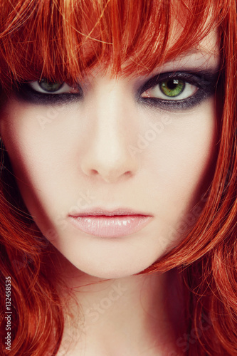 Vintage style close-up portrait of young beautiful green-eyed girl with red hair and stylish smoky eyes makeup