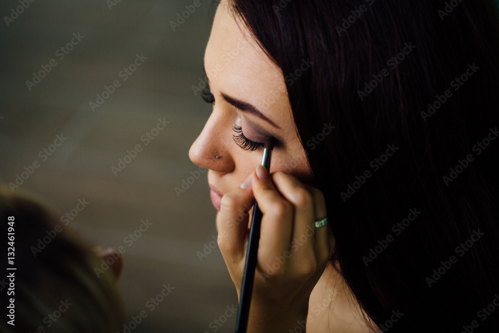 Make-up artist hand applying bright base color on model's face and holding a brush , close . Make-up artist hand applying bright base color on model's face and holding a brush , close .