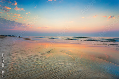 The sky grows vivid and clouds are reflected in the shapes of wet sand at low tide