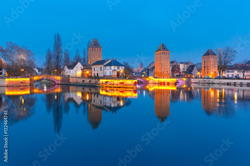 Medieval towers and bridges Ponts Couverts with mirror reflections in Petite France during twilight blue hour, Strasbourg, Alsace, France