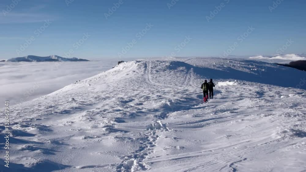 Travellers With Backpacks Make a Winter Hike Above the Clouds With a View of the Distant Peaks by a Coast of the Cloud Sea Travellers With Backpacks Make a Winter Hike Above the Clouds With a View of the Distant Peaks by a Coast of the Cloud Sea