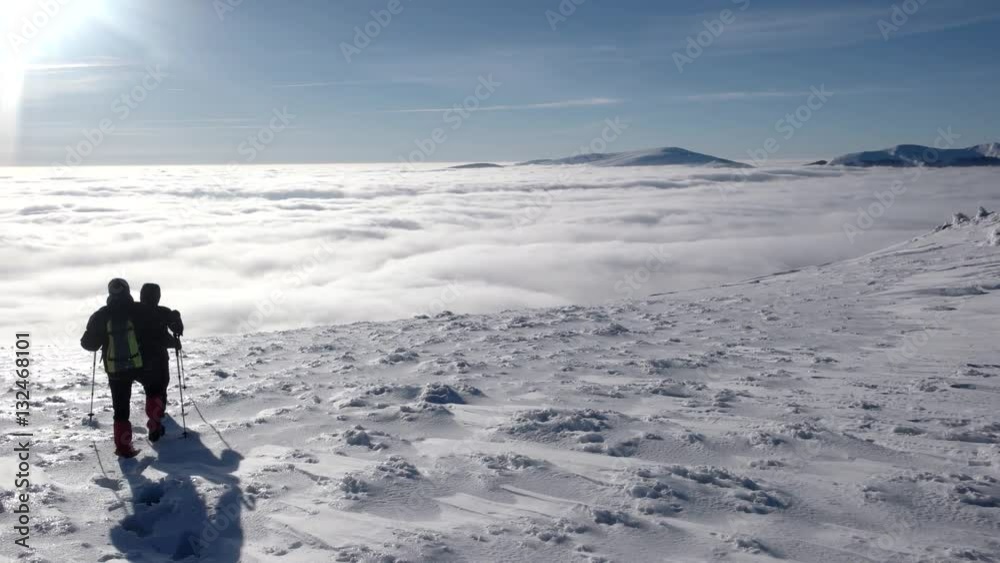 Travellers With Backpacks Make a Winter Hike Above the Clouds With a View of the Distant Peaks by a Coast of the Cloud Sea Travellers With Backpacks Make a Winter Hike Above the Clouds With a View of the Distant Peaks by a Coast of the Cloud Sea
