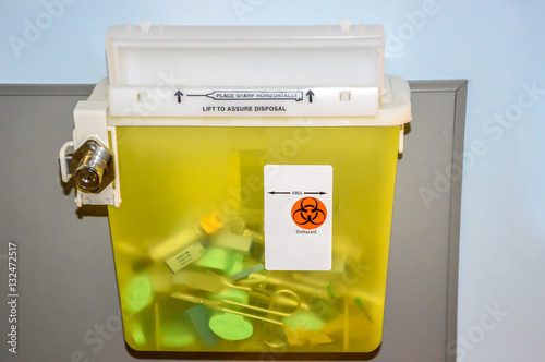 Photo of a locked yellow sharps container with used syringes, needles and scissors.