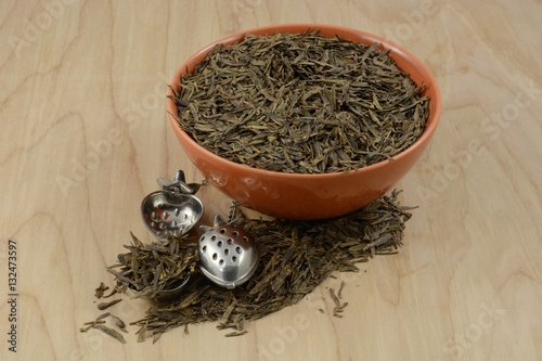 Bowl of dry loose lung ching Chinese green tea leaves and two tea ball infusers photo