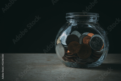 Coins in the bottle on the wooden table with black background in