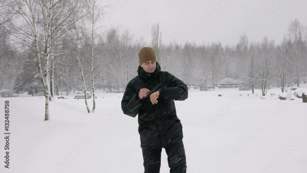 A man checks the messages on the smart watch in the winter snowy forest. Big snowfall. He dictates a voice response to the clock. A man dressed in a dark warm jacket. A man checks the messages on the smart watch in the winter snowy forest. Big snowfall. He dictates a voice response to the clock. A man dressed in a dark warm jacket.
