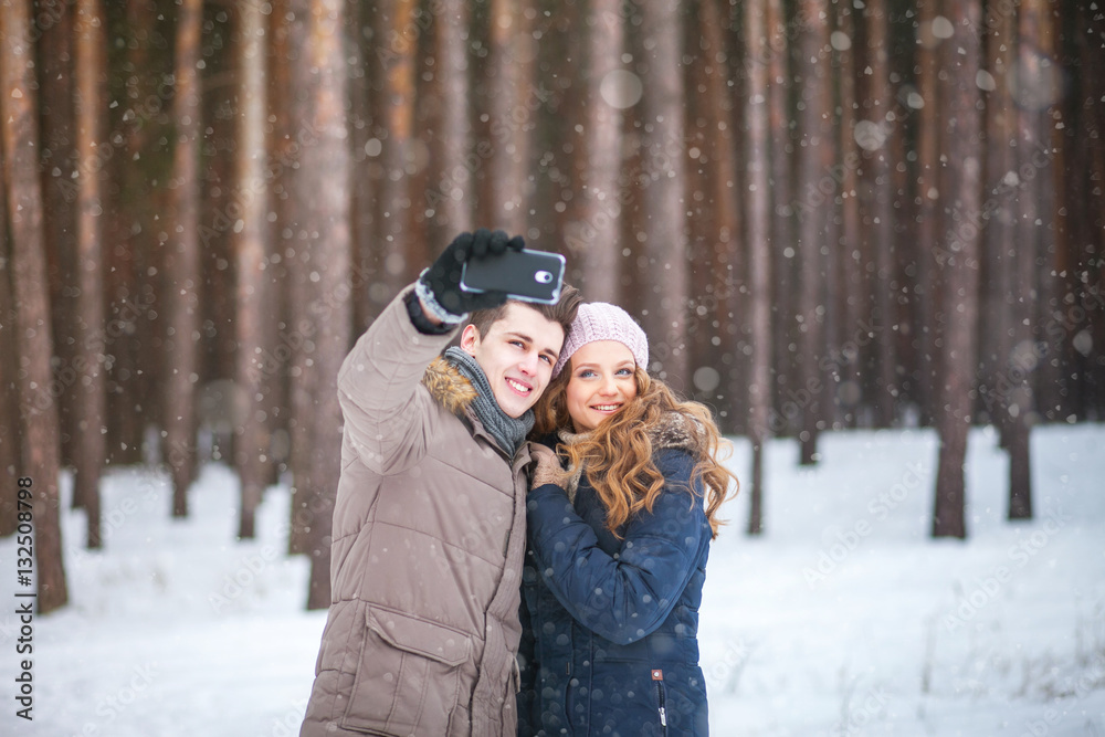 Fototapeta premium people,season,love,technology and leisure concept - happy couple taking picture with smart phone self ie stick on over winter background 