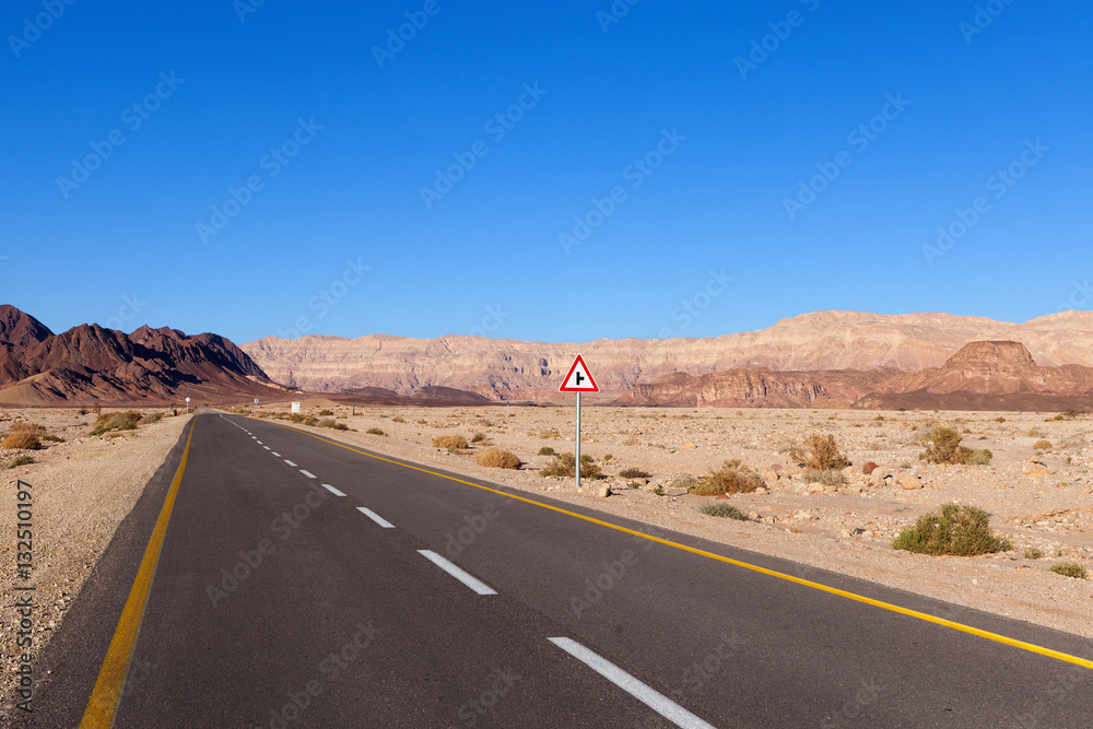 Empty desert road with mountains and blue sky in the background