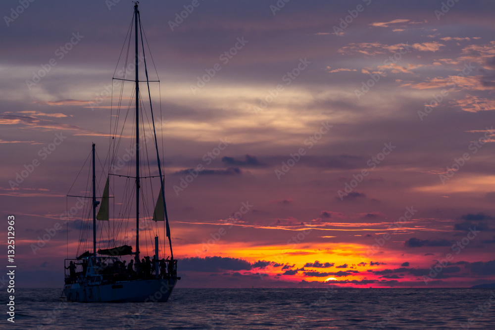 Fototapeta premium Silhouette of a sailboat against colorful vivid sunset sky