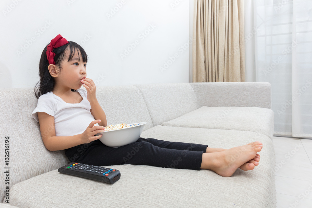 Happy Asian Chinese little girl eating popcorn on the sofa Happy Asian Chinese little girl eating popcorn on the sofa