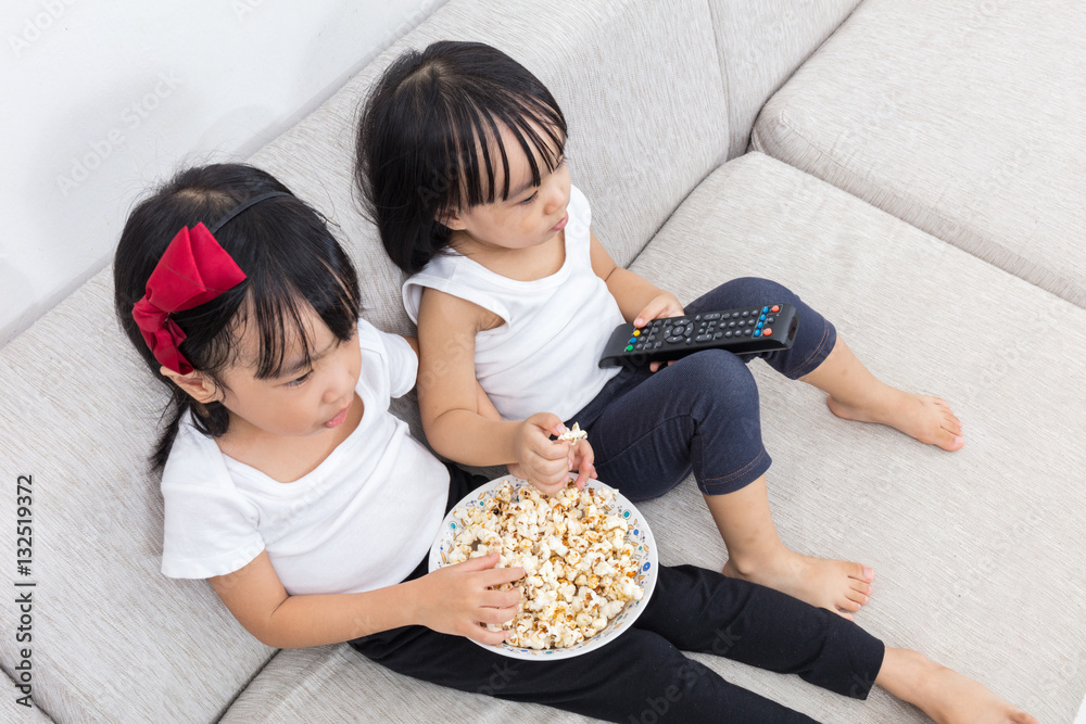 Asian Chinese little sisters eating popcorn on the sofa Asian Chinese little sisters eating popcorn on the sofa