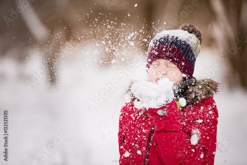 Portrait of cute kid boy blowing snow from his hands on a winter day. Child playing outdoors. Lifestyle concept
