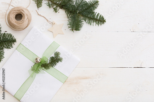 Christmas gift box with tag. New Year present in white box with fir branches at white wooden table. Flat lay with copy space. Celebration, holiday season and winter concept