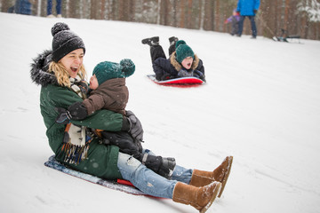 Mother and little toddler boy sliding down the hill in the winter forest and having fun with snow. Family enjoying winter. Child and woman outdoors. Winter, Christmas and lifestyle concept.