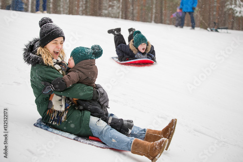Mother and little toddler boy sliding down the hill in the winter forest and having fun with snow. Family enjoying winter. Child and woman outdoors. Winter, Christmas and lifestyle concept.