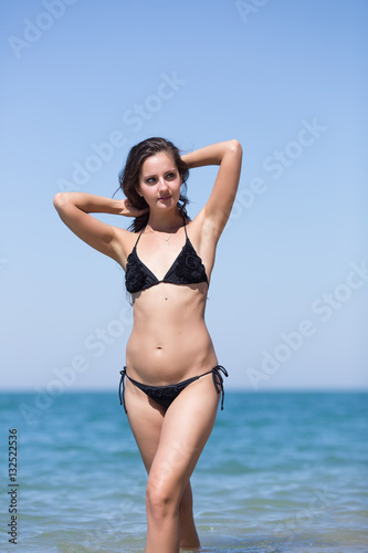 Girl in bikini stands with arms raised