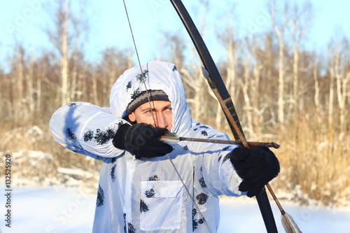 Охотник с луком и стрелами в маскхалате в зимнем лесу