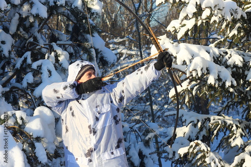 Охотник с луком и стрелами в маскхалате в зимнем лесу